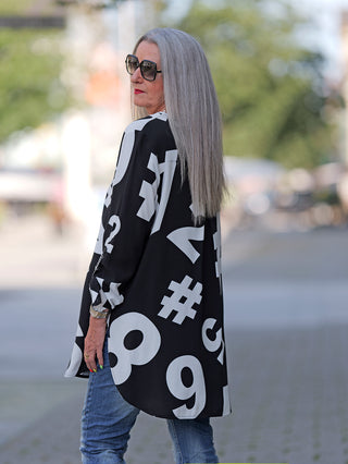 Doris Streich Bluse #7 black&white, getragen von einer Frau mit langen grauen Haaren und Sonnenbrille. Die lässige Bluse zeigt einen Allover-Print und ist aus 100% Viskose.