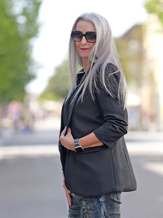 Frau mit langen grauen Haaren trägt den OFF#DLY Blazer Pamela schwarz, sportiver Schnitt mit 3/4 Ärmeln. Der Blazer ist ungefüttert und besteht aus Viskosemischung.