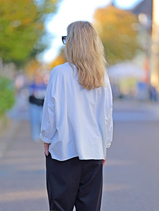 Frau von hinten in einem OFF#DLY Shirt Ulli weiß, leichtem Vintage-Design mit Rundhals, aus Baumwolle und Elastan. Sie trägt eine weiße Bluse, passend bis Größe 40.