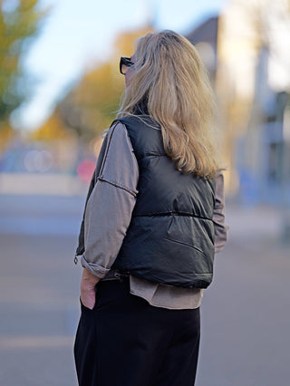 Eine Frau trägt die OFF#DLY Wendeweste Anita black mit Stehkragen. Die Weste hat seitliche Taschen und wird von einem Modell mit langen, blonden Haaren und Sonnenbrille präsentiert.