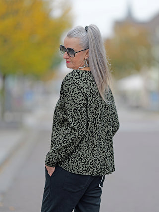 Frau mit grauen Haaren trägt das OFF#DLY Shirt Cindy khaki mit Rundhalsausschnitt und Leopardenmuster. Sie trägt Sonnenbrillen und hat eine Hand in der Tasche.