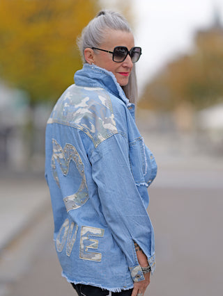 Frau trägt das OFF#DLY Denimshirt Camo mit Nieten und aufgesetzten Taschen, kombiniert mit Sonnenbrille und lässigem Stil.