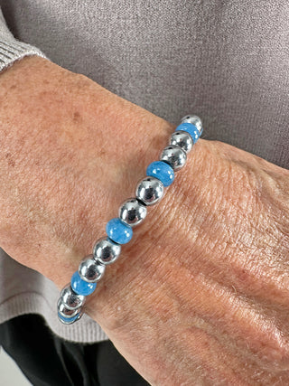 Glam & Rock Armband Edelstahl hellblau, elastisch, auf einem Handgelenk getragen. Silberne und blaue Elemente aus Edelstahl und Edelstein sind sichtbar. Durchmesser ca. 5 mm, Größe One Size.