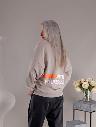 Frau trägt Liv Bergen Ella Dream noisette Sweatshirt mit neon Print, steht vor einer Vase mit weißen Rosen. Lockerer Rundhalssweater, Modelgröße S, Material Baumwolle-Polyester.