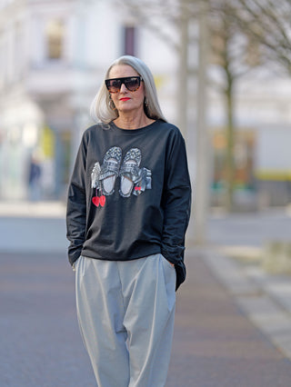 Frau trägt OFF#DLY Sweat Schuh black mit Glanzprint, oversized und gerade geschnitten, passend bis Größe 44. Kombiniert mit Sunglasses für einen modischen Streetstyle-Look.