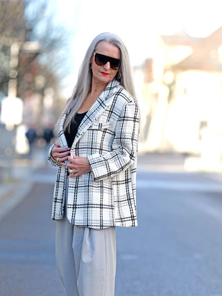 Frau trägt den OFF#DLY Blazer Birte black/white mit Karomuster und Knopfleiste, dazu Sonnenbrille. Der Blazer hat Brusttaschen und eine gerade Passform.