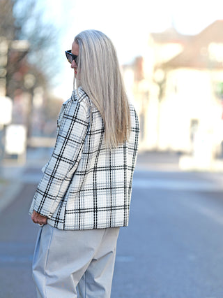 Frau mit langen grauen Haaren trägt den OFF#DLY Blazer Birte black/white mit Karomuster und Knopfleiste, ergänzt durch Brusttaschen, im Street-Fashion-Stil.