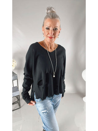 Philomena Pulli 115 black: Frau trägt schwarzen, boxy geschnittenen Pullover mit Löchern, der hinten länger ist. Perfekt für einen lässigen Look.