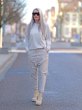 Frau mit langen grauen Haaren trägt OFF#DLY Jogger Pant Tina beige, lässige Baggy Jogger mit Gummibund und Kordelzug, kombiniert mit weißen Stiefeln und Sonnenbrille.