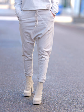 Eine Person trägt die OFF#DLY Jogger Pant Tina beige mit weißer Stiefel, zeigt Baggy-Passform und seitliche Einschubtaschen, ideal für einen lässigen Look.