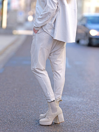 OFF#DLY Jogger Pant Tina beige, getragen von einer Person, zeigt eine lässige Baggy-Passform mit Gummibund und Kordelzug. Die weißen Stiefel ergänzen den entspannten Streetwear-Look.