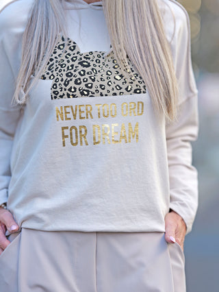 Frau trägt OFF#DLY Hoody Tee Dream beige mit goldener Schrift auf der Vorderseite. Der leichte Hoody hat eine gerade Passform und besteht aus Baumwolle-Elastan-Mix.