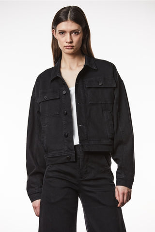 Frau trägt Thom Krom Jacke WJ 210 black, eine taillierte, oversized Jeansjacke mit elastischem Denimstoff und Knöpfen, sichtbar sind Taschen und Kragen.