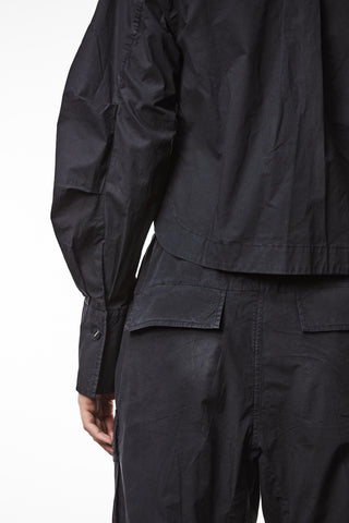 Thom Krom Bluse WH 16 black, getragen von einer Person, zeigt eine gerade Passform mit verdeckter Knopfleiste. Plissee-Details an den Ärmeln und Taschen sind sichtbar.