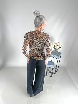 Frau trägt OFF#DLY Longsleeve Tiger beige/black mit Leopardenmuster, verziert mit Strasssteinen und Kunstperlen, vor einem Tisch mit weißen Rosen in einer Glasvase.