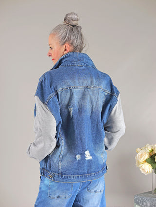 Frau in OFF#DLY Denim Jacket Conny midblue/grey mit Sweatärmeln, oversized Passform. Sie hält einen Blumenstrauß aus weißen Rosen.