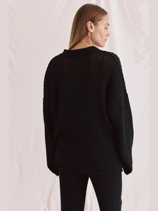 Cotten Candy Pullover Martha black: Frau im schwarzen, oversized Strickpullover mit weiten Ärmeln und turtleneck, aus 100% Baumwolle. Ideal für Sommer, maschinenwaschbar, moderner Stil. Model trägt Größe S bei 1,70 m.