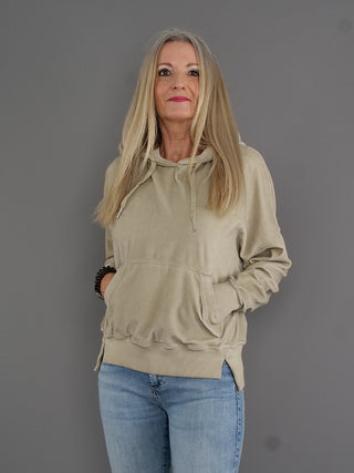 Frau mit blondem Haar trägt den True Religion Hoodie Cold Dye Fossil im Boxy-Look, mit breiten Bündchen und Kängurutasche, aus kuscheligem Frottee-Material.