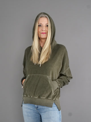 Frau mit langen blonden Haaren trägt den True Religion Hoodie Cold Dye Leaf mit Kapuze, leicht oversize, Boxy-Look und Kängurutasche, aus weichem Frottee-Material.