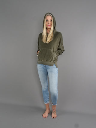 Frau trägt True Religion Hoodie Cold Dye Leaf in kuscheliger Frottee-Optik mit breiten Bündchen und Kängurutasche, leicht oversize und im Boxy-Look, stehend vor grauer Wand.