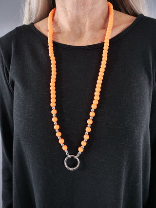 Glam&Rock Kette orange, getragen von einer Person. Die neonfarbene Halskette besitzt einen Karabiner zum Einhängen von Anhängern. Sie ist ein modisches Accessoire, das den Hals elegant betont.